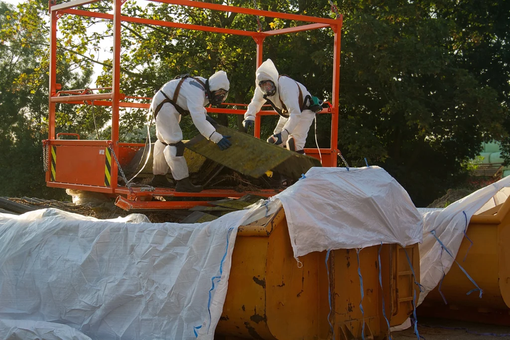 Two workers in protective suits safely disposing of asbestos material for asbestos removal services